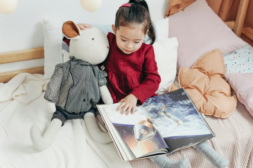 pexels-photo-3661473-3661473-1 Child reading a picture book with a stuffed toy in a cozy bedroom setting.
